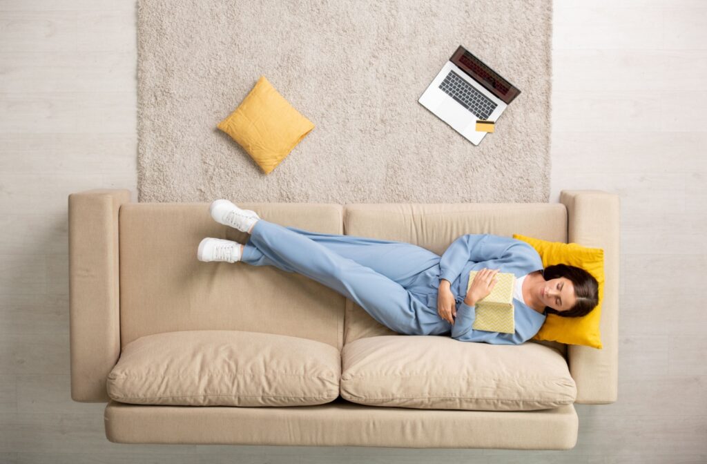 A bird’s-eye view of a person lying on the couch, recovering after a tooth extraction.