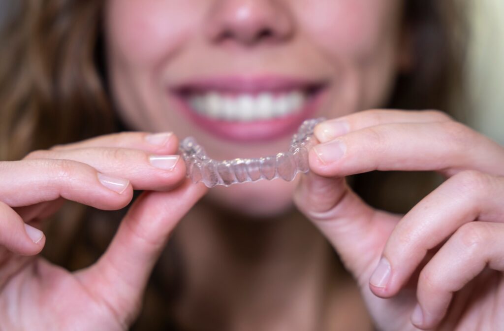 A close up of two hands holding out an Invisalign bottom aligner as an option for adults looking for orthodontic treatment.