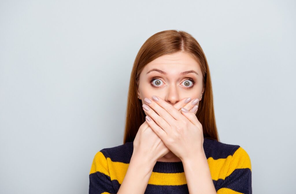 Woman covering her mouth with both hands, possibly reacting to a dental emergency.