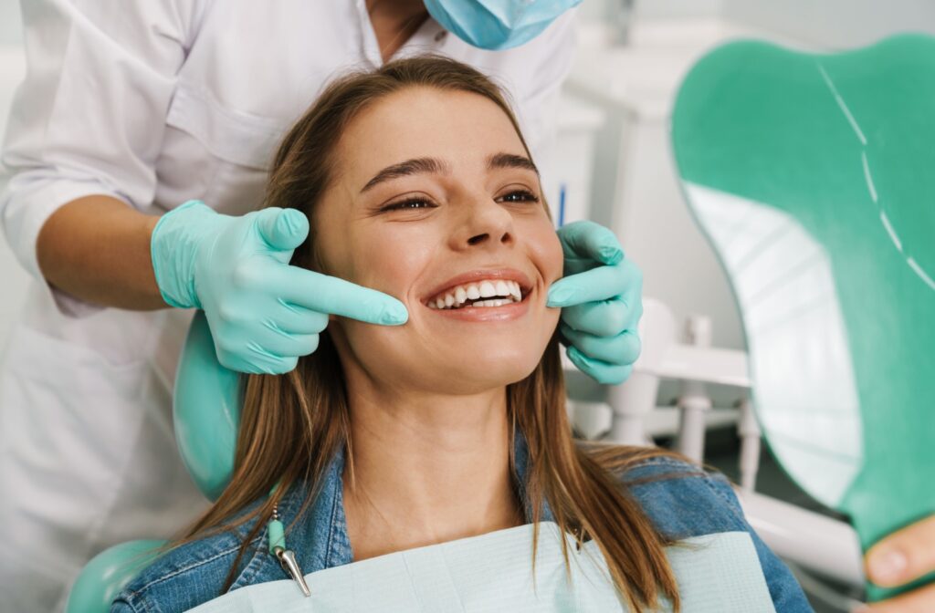 Smiling patient in a dental chair as a dentist in gloves checks her teeth during an exam.